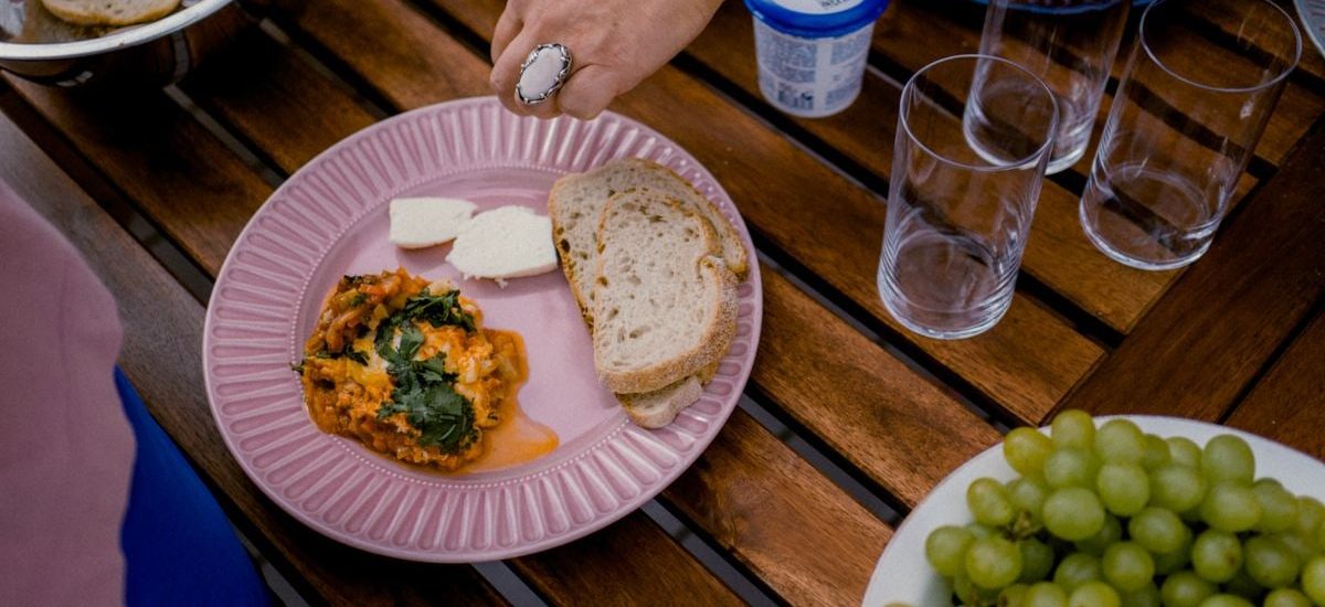 A casual outdoor dining table with bread, greens, and a side dish for brunch.
